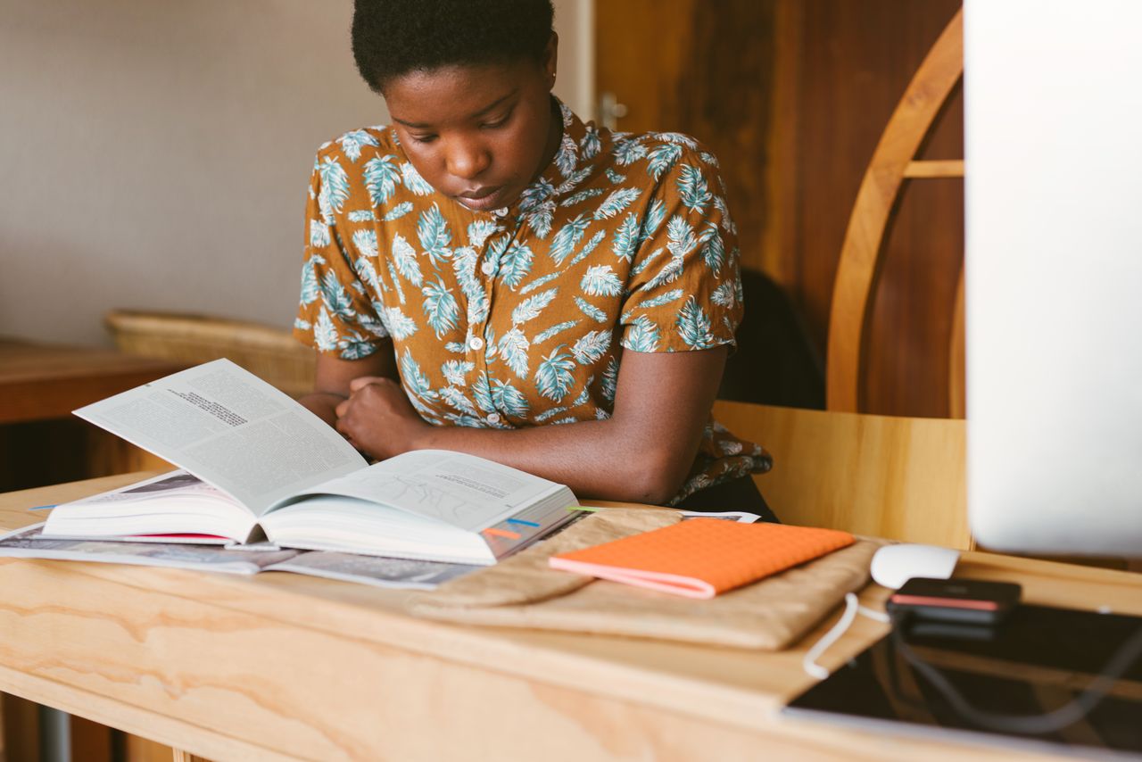 A young woman studies a book at her desk in a warm, indoor setting, illustrating a calm study environment.