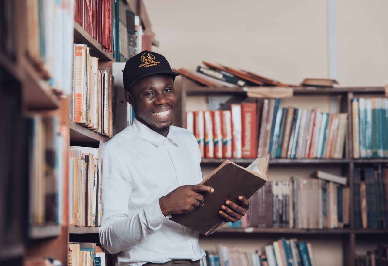 A joyful man reading in a Ghanaian library, symbolizing education and knowledge.