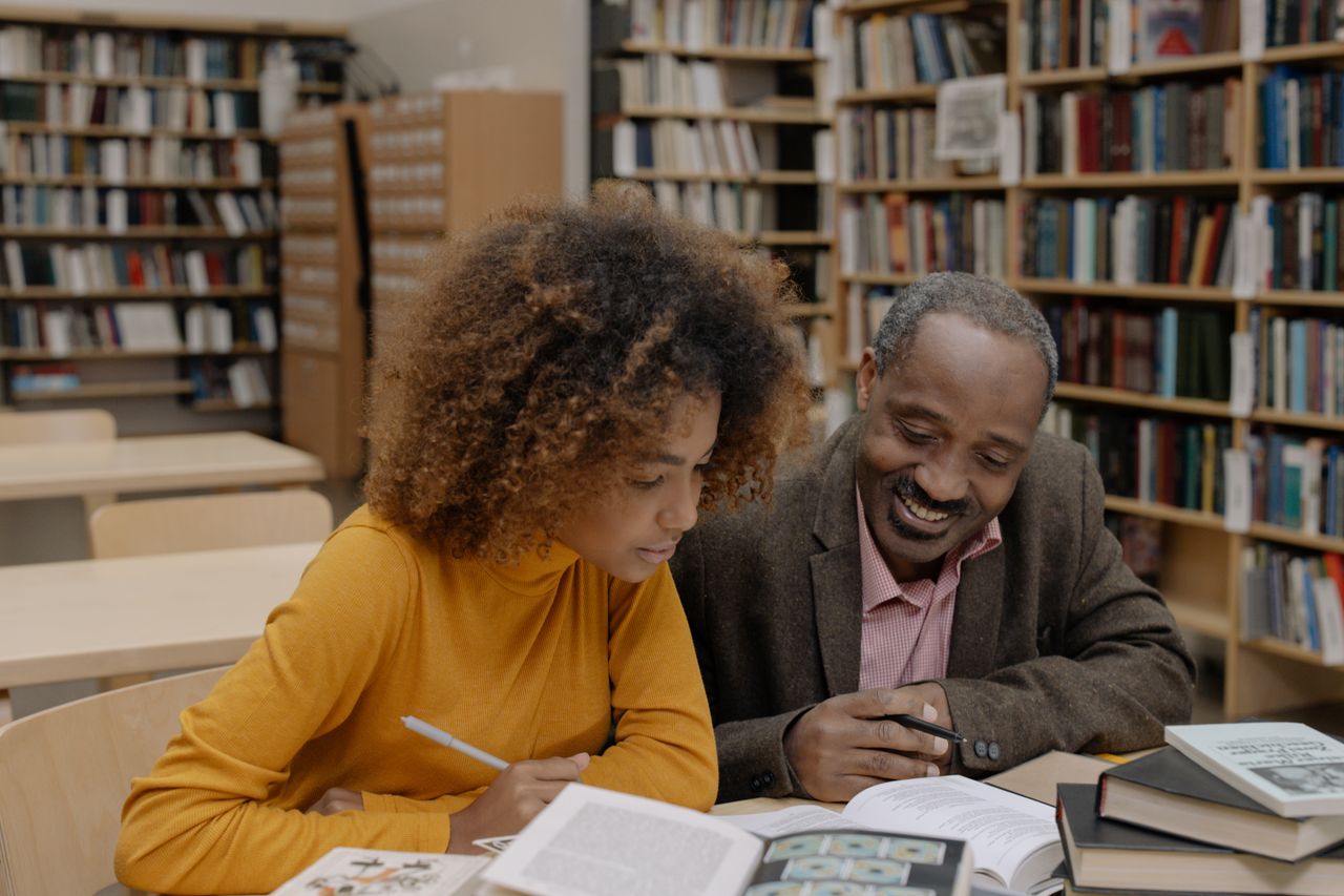 Two adults studying in a library, surrounded by books, enhancing education and knowledge.